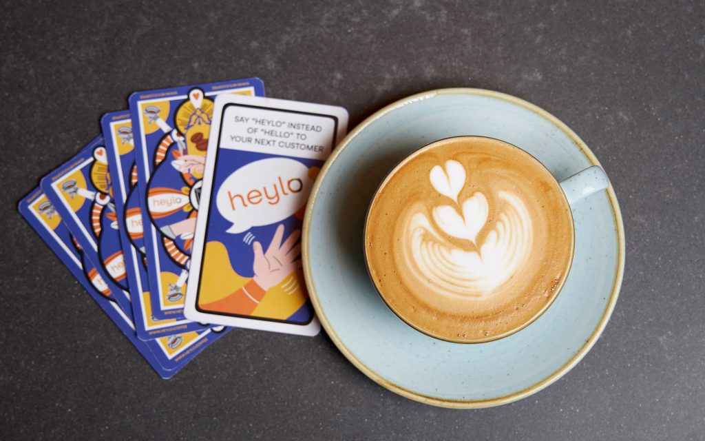 A milk-based coffee beverage with latte art next to some Heylo cards.