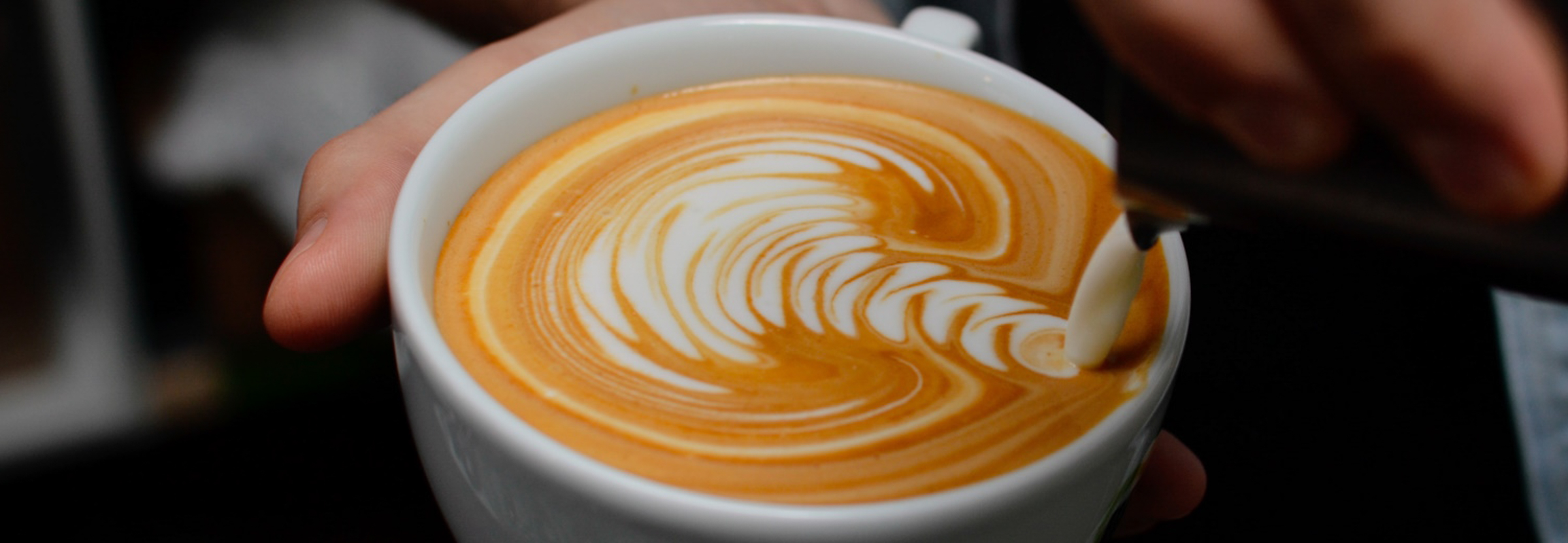 A barista prepares a cup of coffee featuring latte art.