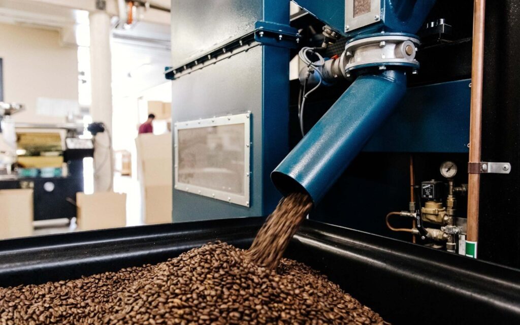 A machine dispenses roasted coffee beans in a roastery.