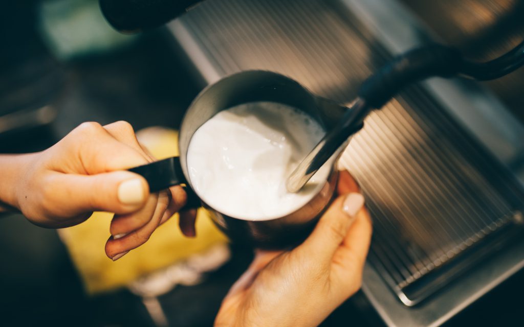 A barista uses a steam wand to foam milk for coffee.